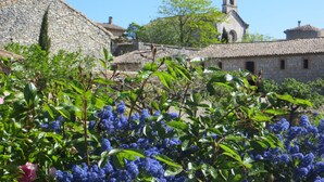 A stone building with a bell tower, surrounded by greenery and flowering plants. - COTTAGE WITH HEATED POOL - MAS IN THE GARRIGUE D'UZES (Fons-Sur-Lussan)
