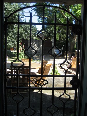 Una reja de hierro forjado con vista a un patio que tiene una mesa y sillas de madera, una hamaca y un muro de piedra.