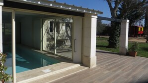 A covered outdoor pool area with a glass door leading to a patio with a table and chairs. - COTTAGE WITH HEATED POOL - MAS IN THE GARRIGUE D'UZES (Fons-Sur-Lussan)