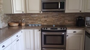 A kitchen with white cabinets, a microwave, an oven, and a tiled floor.