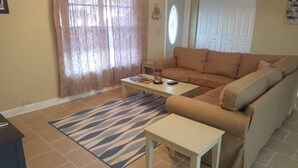 A living room with a beige sofa, a white coffee table, a zebra-patterned rug, and a small white table.