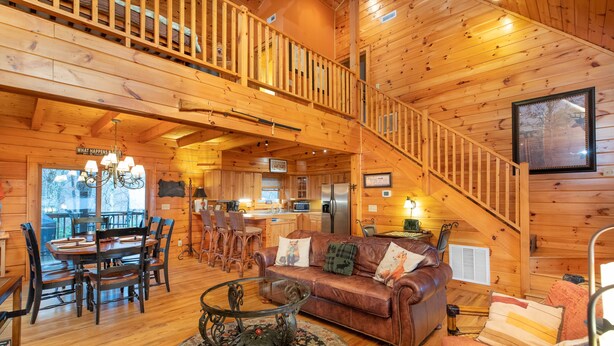 Ein Interieur einer Holzhütte mit Essbereich, einem Wohnzimmer mit Sofa und Couchtisch sowie einer Treppe.