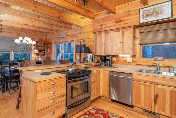 A wooden cabin-style kitchen with a central island, built-in oven, dishwasher, and wooden cabinets. - Mountain Majesty: Luxury Log Cabin Retreat with Spectacular Views and a Hot Tub (Waynesville)