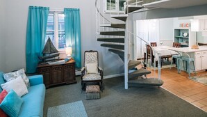 A spacious living area with a blue sofa, a patterned rug, a wooden side table, a sailboat model, and a spiral staircase leading to an upper level. - Adjacent to beaches, 3 minute walk to downtown, Quiet Atmosphere, FREE WIFI (Sodus Point)