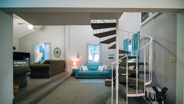 A living room with a spiral staircase, a sofa, a television, and a lamp. - Adjacent to beaches, 3 minute walk to downtown, Quiet Atmosphere, FREE WIFI (Sodus Point)