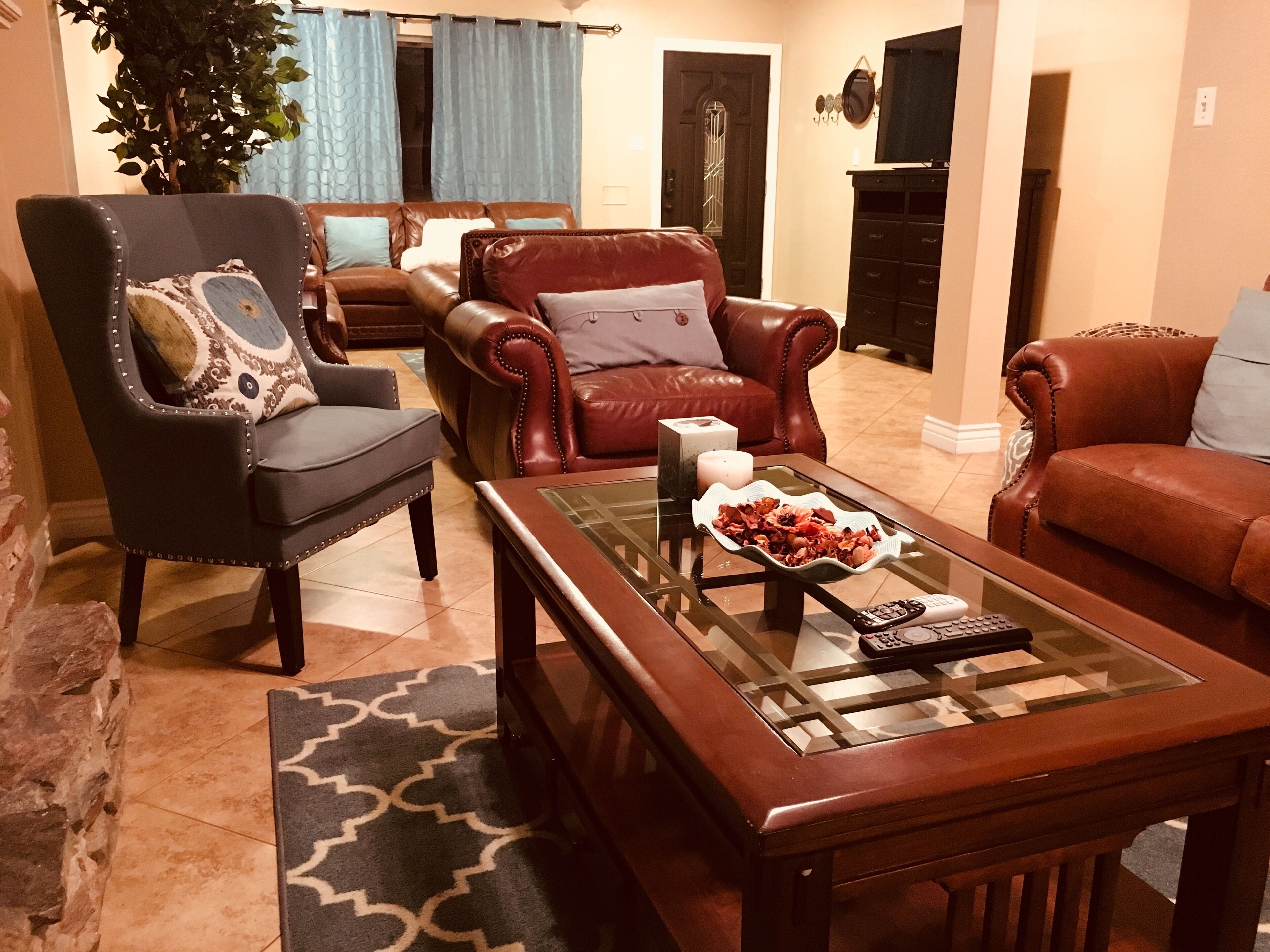 Een woonkamer met een bruine leren bank, een zwarte fauteuil en een glazen salontafel met een afstandsbediening.