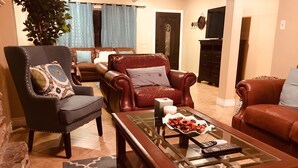Un salon avec un canapé en cuir marron, un fauteuil noir et une table basse en verre sur laquelle se trouve une télécommande.