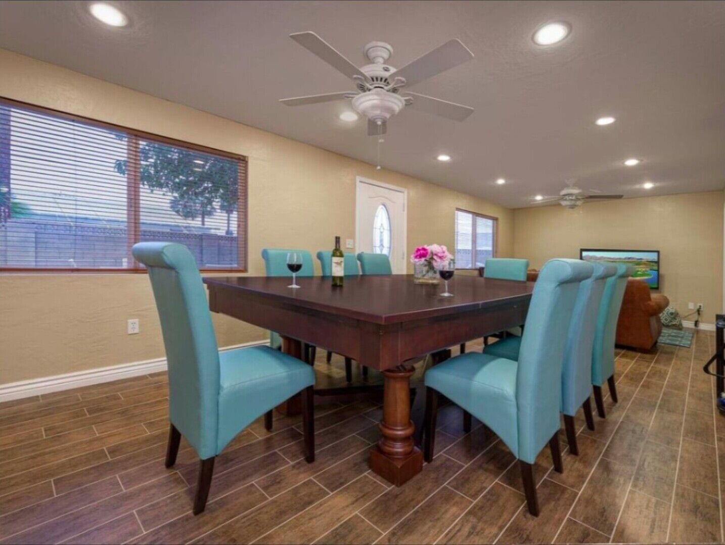 A dining room with a dark wooden table, teal chairs, and a ceiling fan.