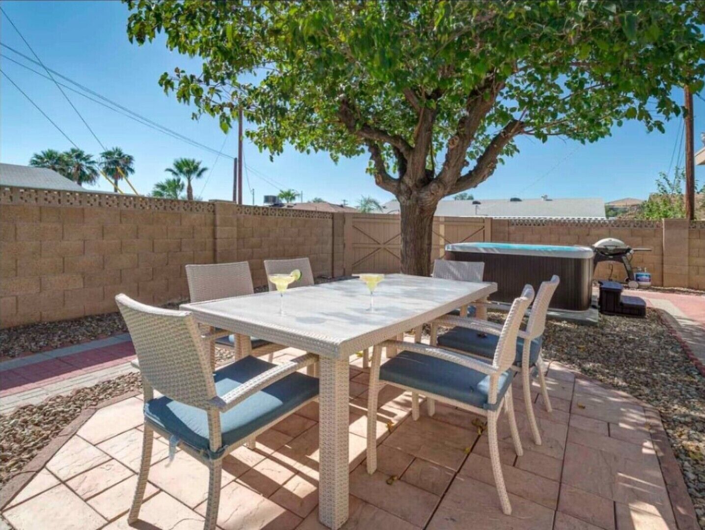 Eine Terrasse mit Tisch und Stühlen, einem Grill und einem Baum, der Schatten spendet.