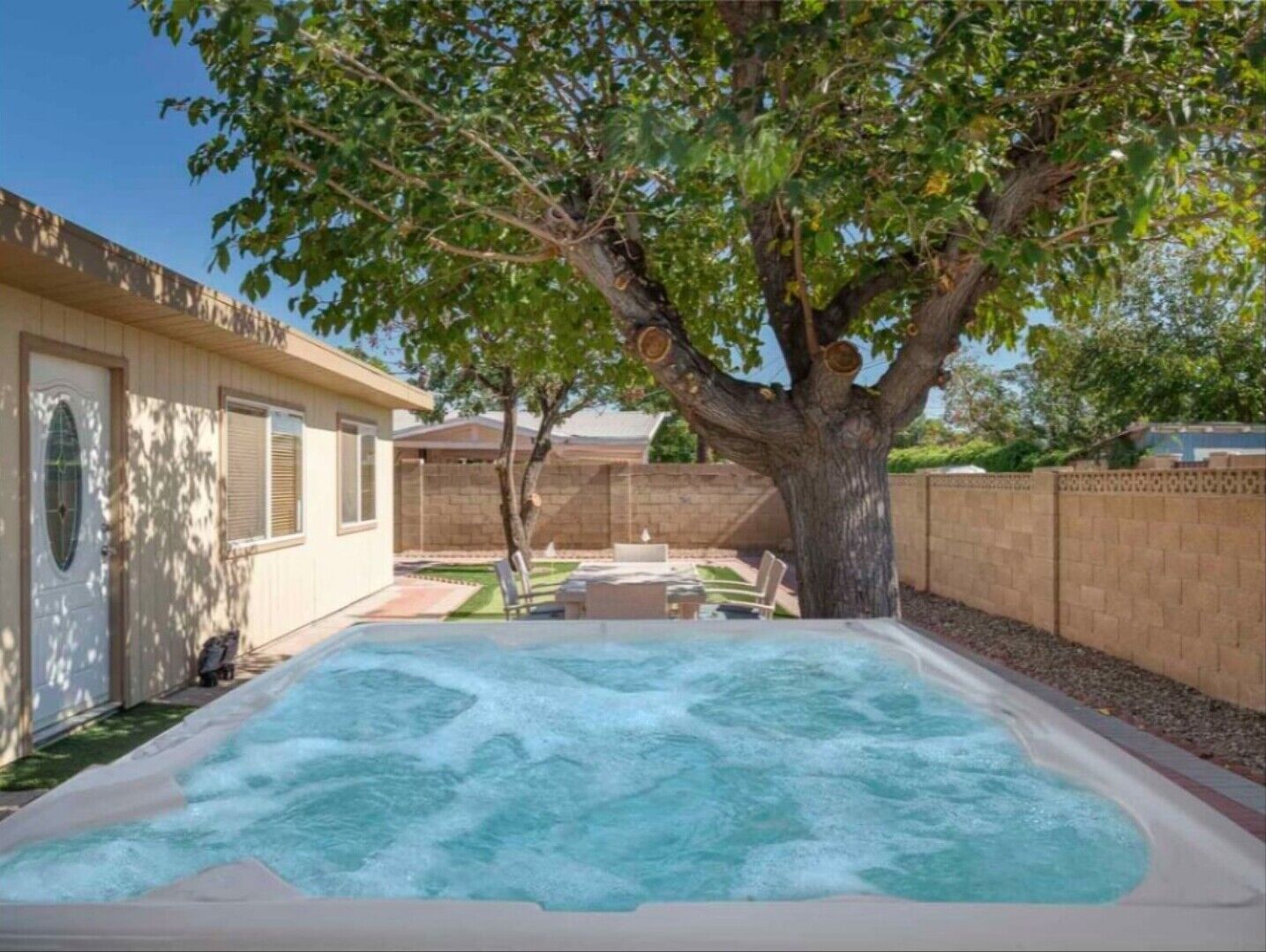 A backyard with a hot tub, a tree, and a patio area.