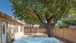 Un jardin avec un jacuzzi, un arbre et un espace patio.