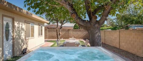 Un patio trasero con un jacuzzi, un árbol y una zona de terraza.