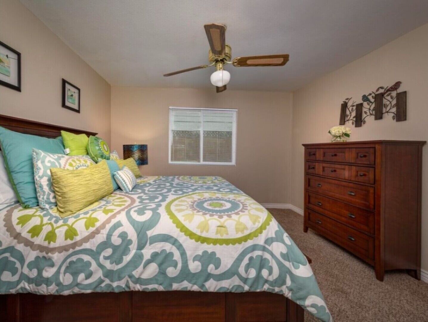 Quarto com cama, penteadeira, ventoinha no teto e janela com persianas.