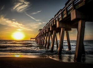 Eine Steg, der sich ins Meer erstreckt, mit untergehendem Sonnenuntergang im Hintergrund.