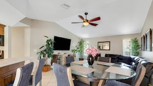 A modern living room with a glass-top dining table, leather sofa, and ceiling fan. - IMMACULATE 3BR 2 BATH PRIVATE POOL HOME MINUTES TO BEACHES, DOWNTOWN.  (Venice)