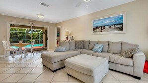 A living room with a beige sectional sofa, a dining table with chairs, a ceiling fan, and a large window overlooking a swimming pool. - IMMACULATE 3BR 2 BATH PRIVATE POOL HOME MINUTES TO BEACHES, DOWNTOWN.  (Venice)