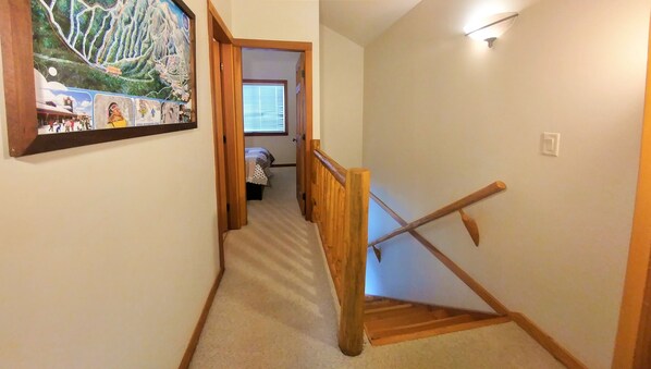 A hallway with a wooden handrail, carpeted floor, and a framed map on the wall.