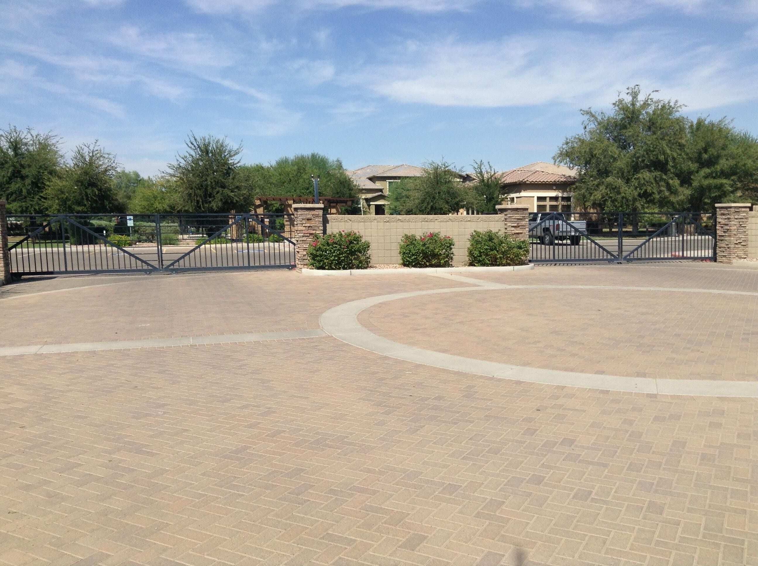 A paved courtyard with a curved pathway, surrounded by a stone wall and metal gates.