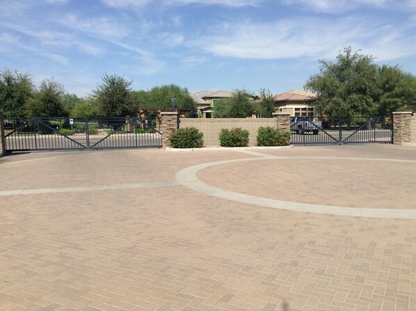 A paved courtyard with a curved pathway, surrounded by a stone wall and metal gates.