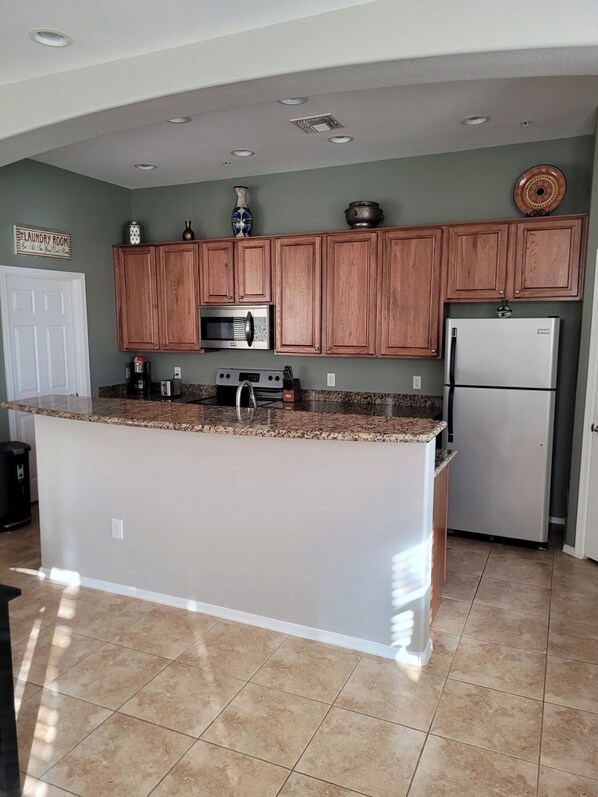 A kitchen with wooden cabinets, a stainless steel refrigerator, and a granite countertop island.