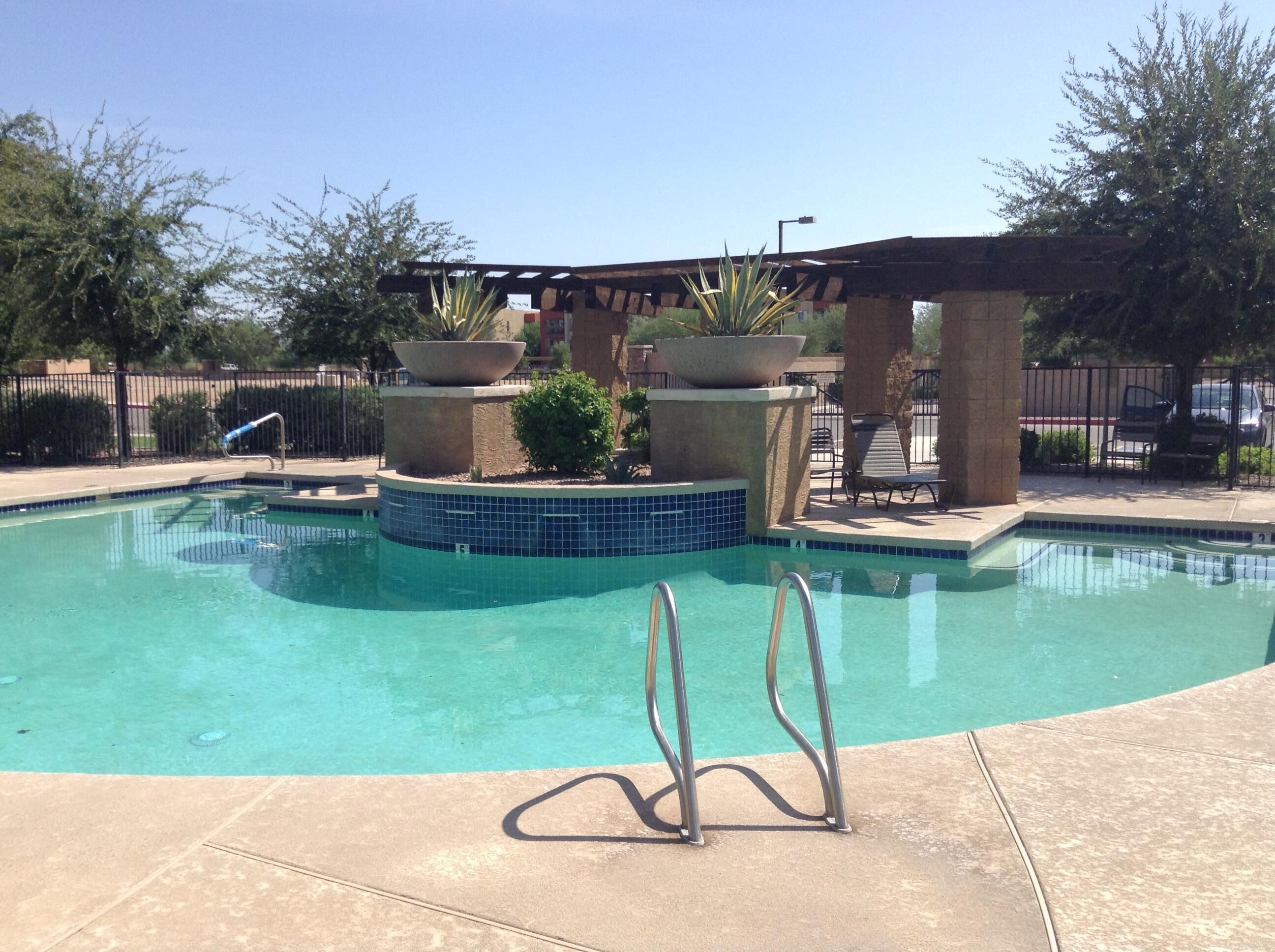 A clear swimming pool with a tiled edge, a metal ladder, and a pergola structure.
