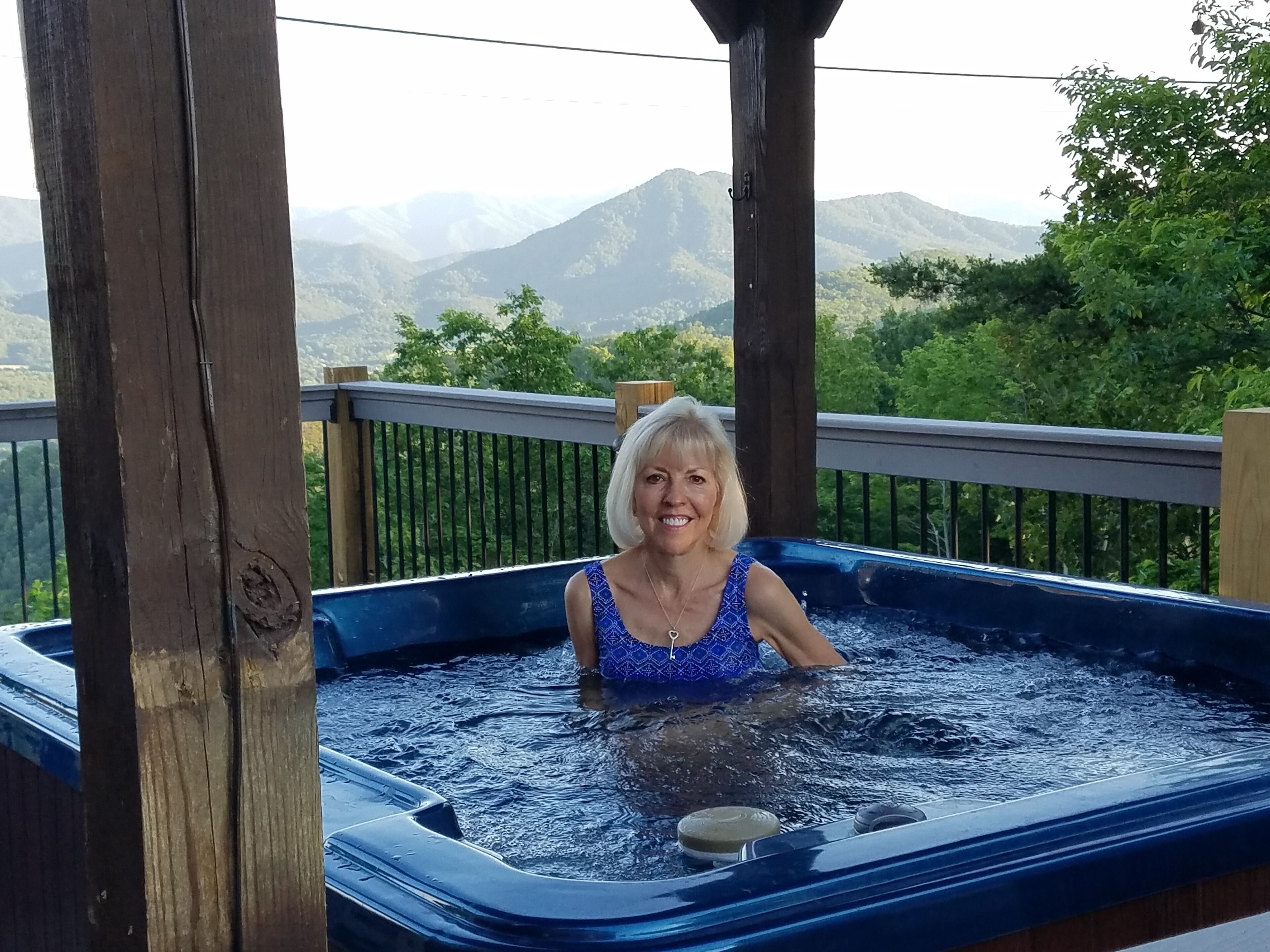 Una persona en un jacuzzi en un balcón con vistas a montañas.