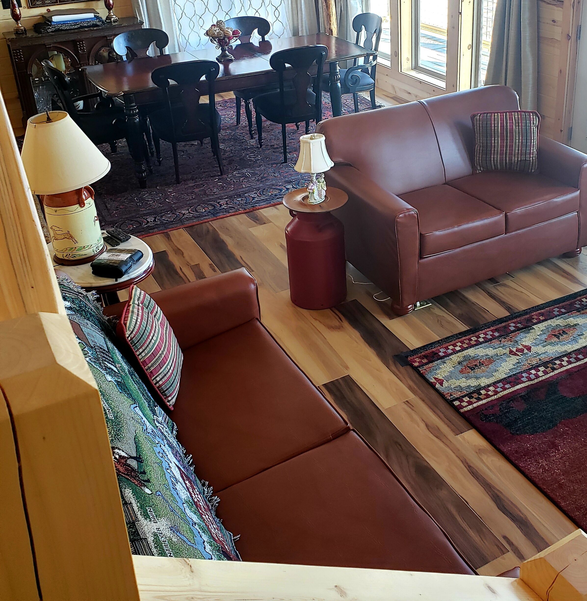 Un salon chaleureux avec un canapé en cuir marron, un tapis à motifs et un coin repas comprenant une table et des chaises en bois.