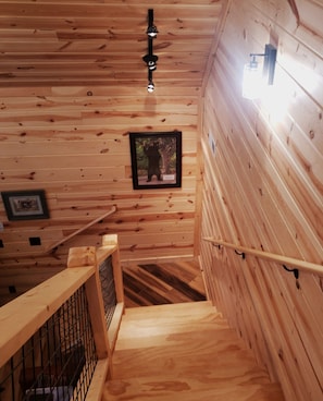 Eine Holztreppe mit Metallgeländer, ein gerahmtes Bild an der Wand und eine Deckenleuchte.