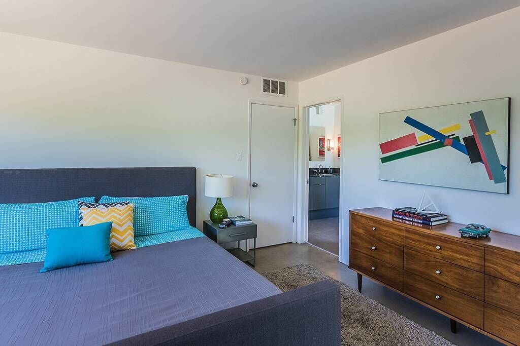 A modern bedroom with a bed, a dresser, and a wall-mounted abstract painting.