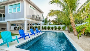 Ein modernes Haus mit Swimmingpool, blauen Stühlen und einer überdachten Terrasse.