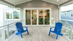 Eine überdachte Veranda mit zwei blauen Adirondack-Stühlen, einer Chandelierleuchtre und Blick in einen Küchenbereich.