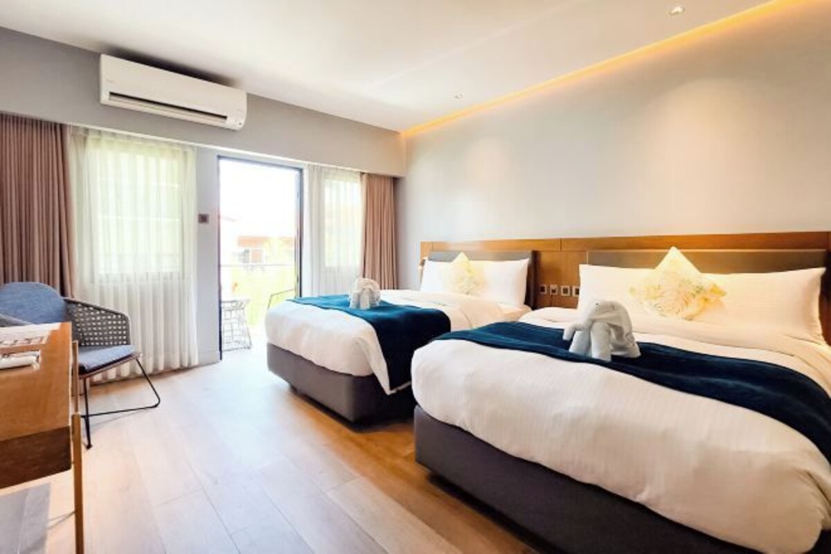 A hotel room with two beds, a desk, and a chair.