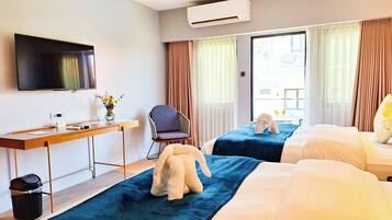A hotel room with two beds, a desk, a chair, a TV, and a view of the outside.