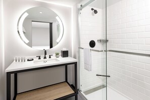 A modern bathroom with a white sink, mirror, and glass shower enclosure.
