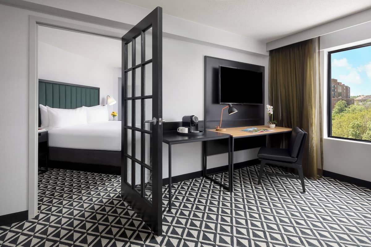 A hotel room with a bed, desk, chair, TV, and large window.