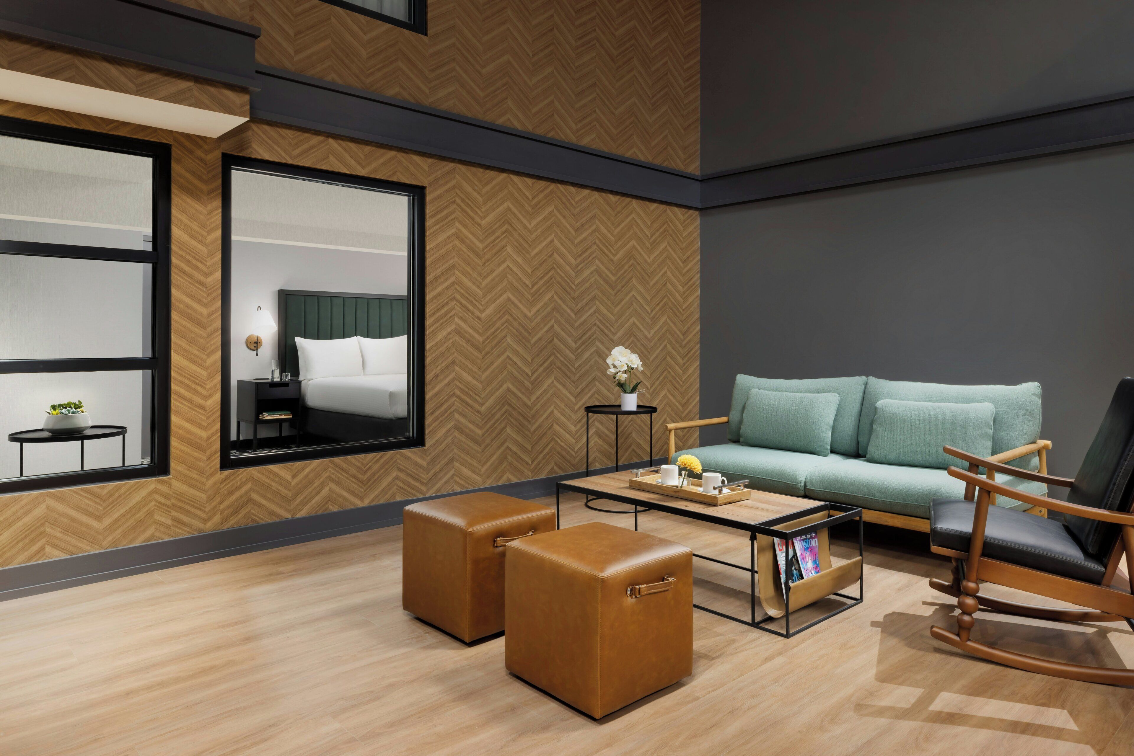 A modern hotel room with a large bed, a sofa, a coffee table, and two ottomans.