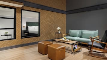 A modern hotel room with a large bed, a sofa, a coffee table, and two ottomans.