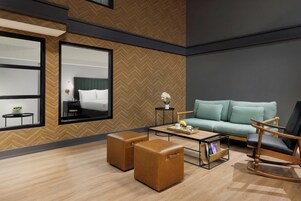 Una habitación de hotel moderna con una cama grande, un sofá, una mesita de café y dos otomanas.