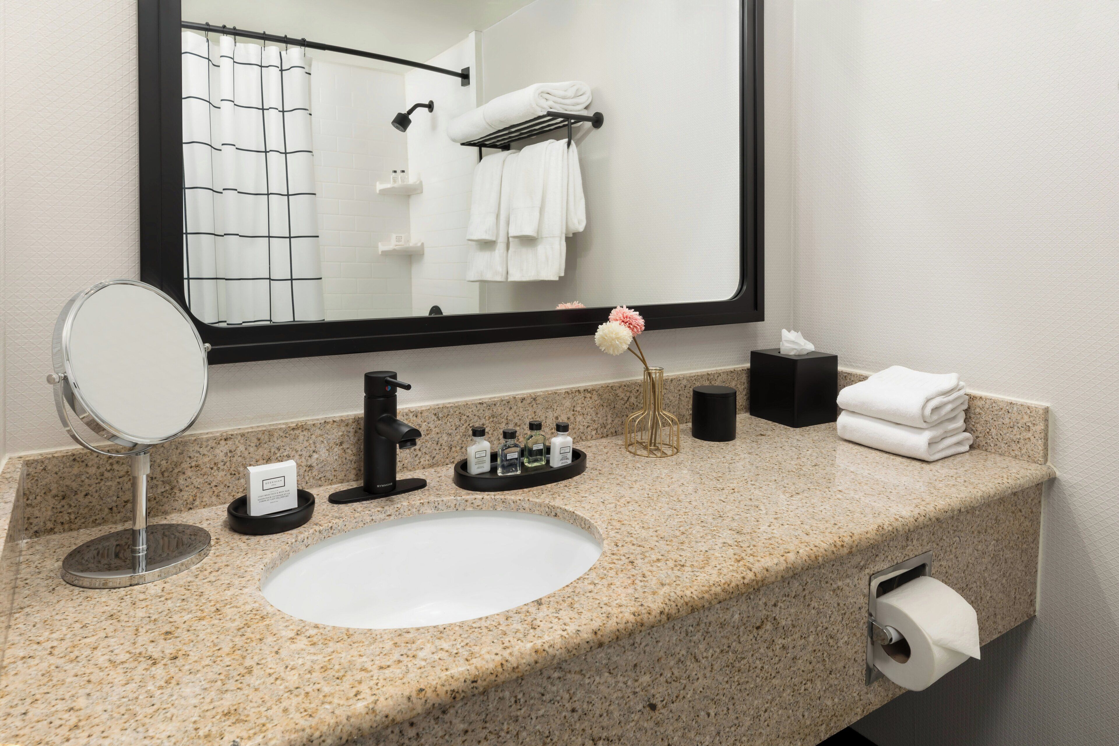 A bathroom with a granite countertop, a white sink, a mirror, a towel rack, and a toilet paper holder.