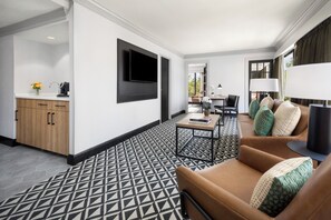 Een moderne hotelkamer met een vloer in geometrisch patroon, een bruine leren bank, een flatscreen televisie aan de muur en een kleine tafel met een lamp.