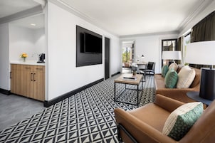 Una habitación de hotel moderna con piso de diseño geométrico, un sofá de cuero marrón, un televisor de pantalla plana montado en la pared y una mesita de noche con una lámpara.