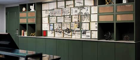 Une bibliothèque aux murs verts, avec des étagères remplies de livres et un bureau équipé d’un ordinateur.