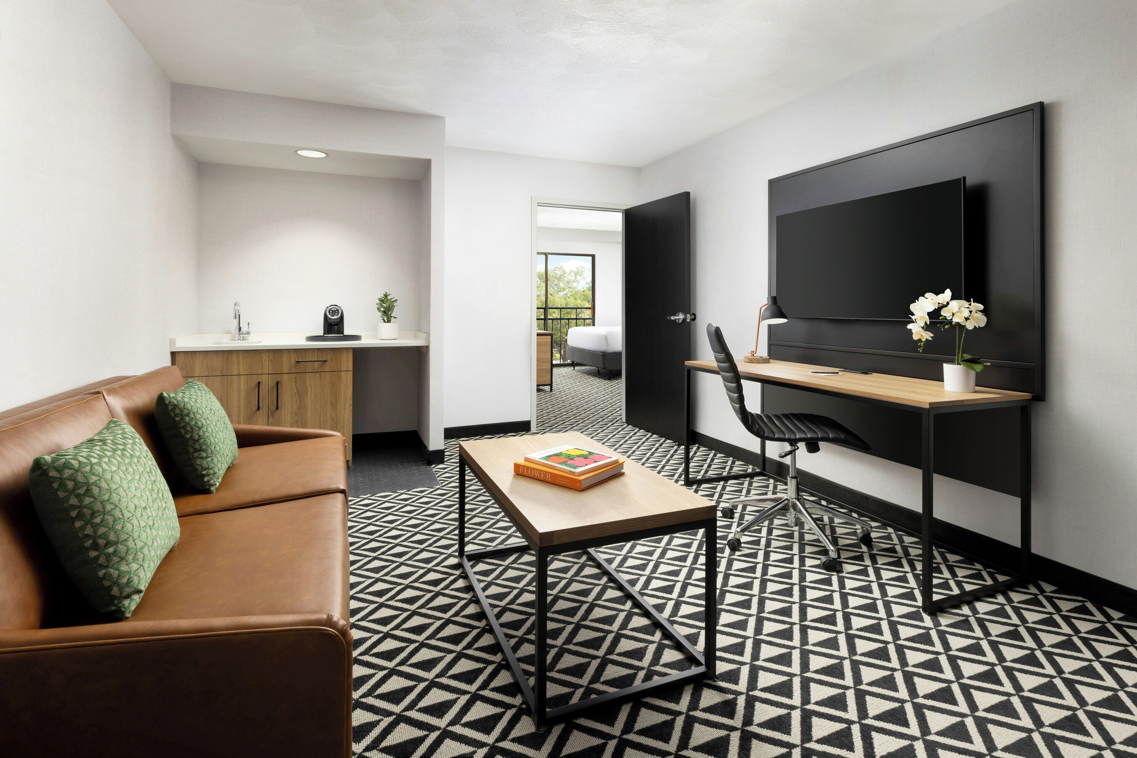 Un espace de vie moderne comprenant un canapé, une table basse, un bureau avec une chaise, un téléviseur à écran plat et un sol à motifs.