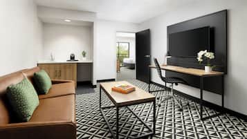A modern living space with a sofa, a coffee table, a desk with a chair, a flat-screen TV, and a patterned floor.