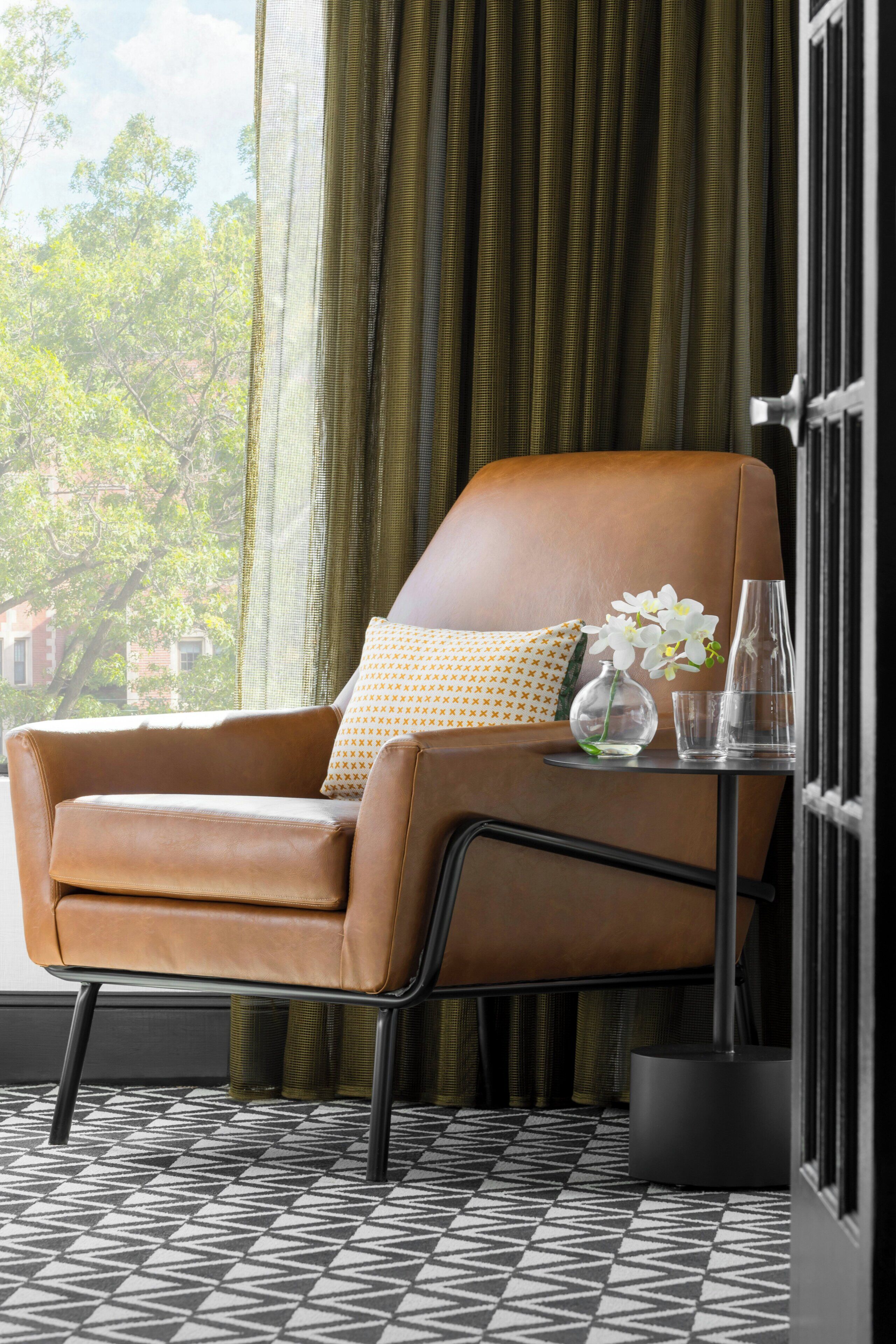 A brown leather armchair with a patterned cushion, a small table with a vase of flowers, and a patterned floor.