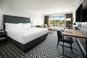 A hotel room with a large bed, a desk with a chair, a television, and a window with a view of buildings. - Arcadian Hotel (Brookline)