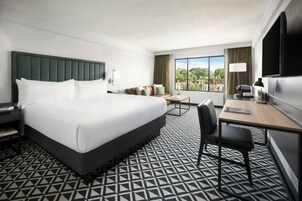 Habitación de hotel con una cama grande, un escritorio con una silla, televisión y ventana con vista a edificios.