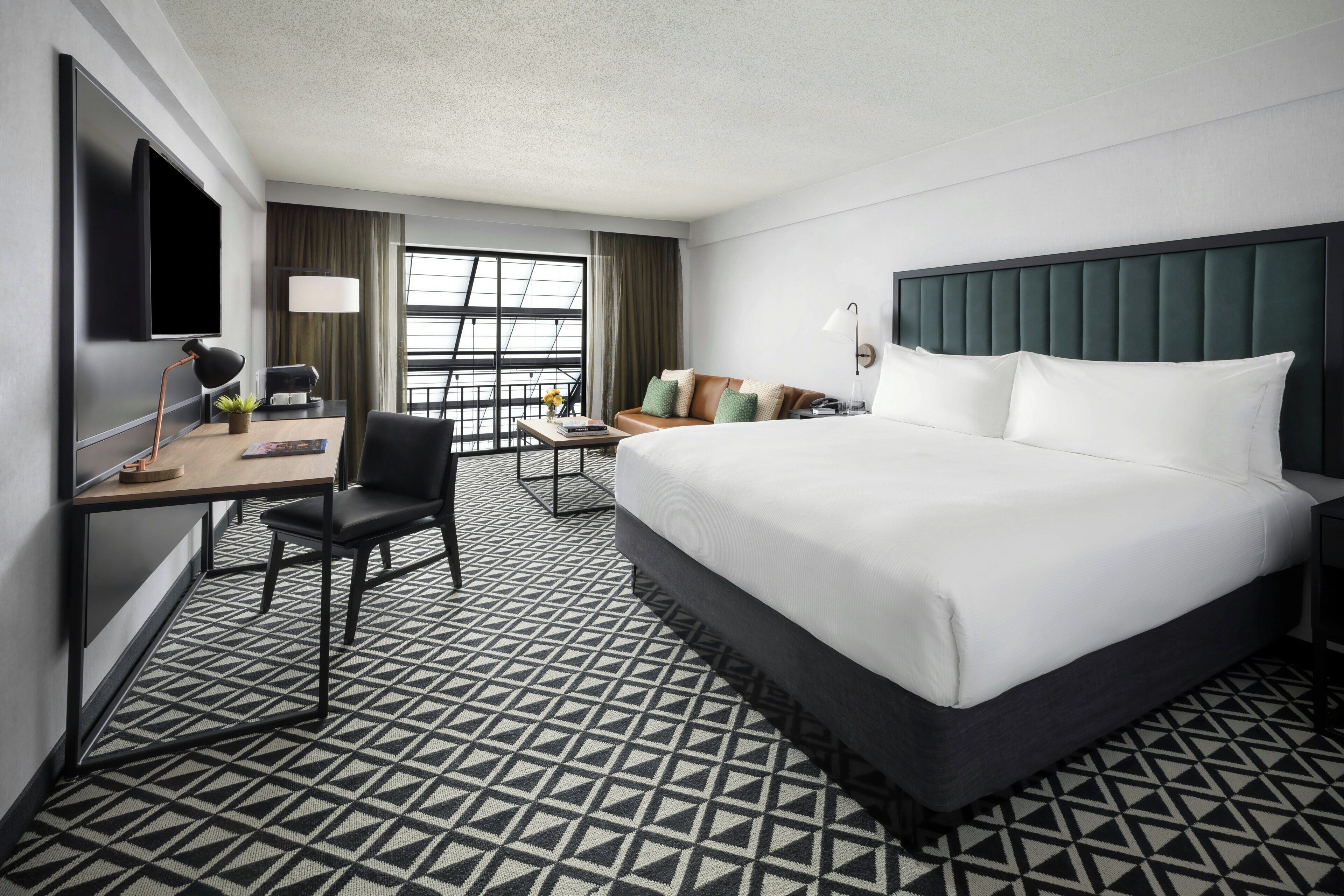 Habitación de hotel con una cama grande, un escritorio con silla, televisión y ventana con cortinas.