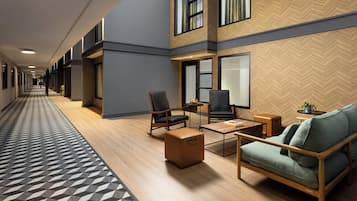 Un hall d’hôtel avec un long couloir, un espace détente doté de canapés et de fauteuils, et un mur orné d’un motif en chevrons.