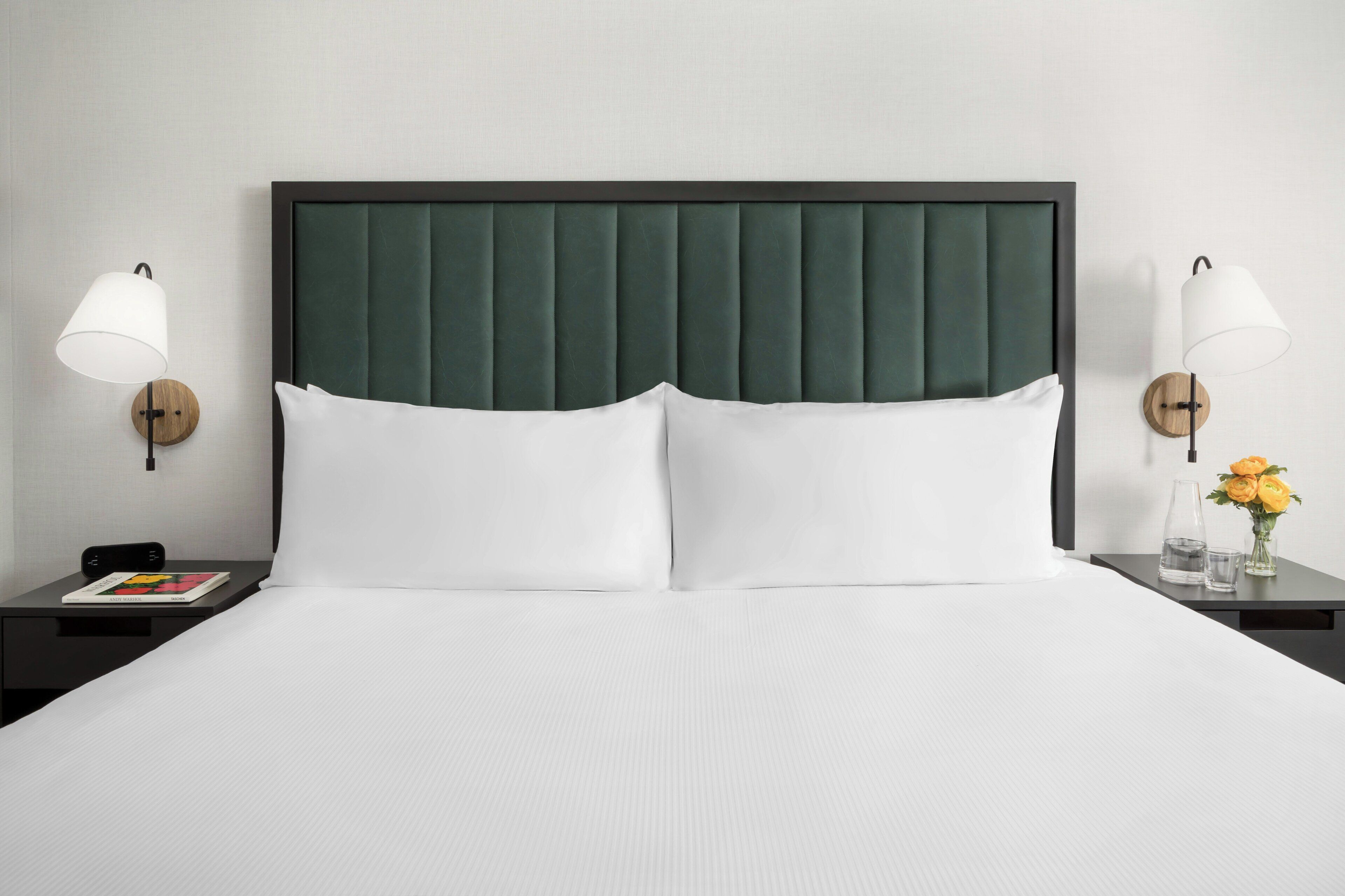A neatly made bed with white linens, flanked by two bedside tables with lamps, and a wall-mounted light fixture.